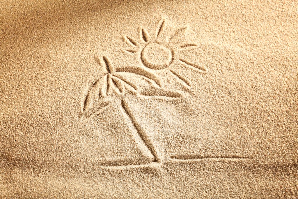 Jemand hat ein fröhliches Strandbild in den Sand gezeichnet.